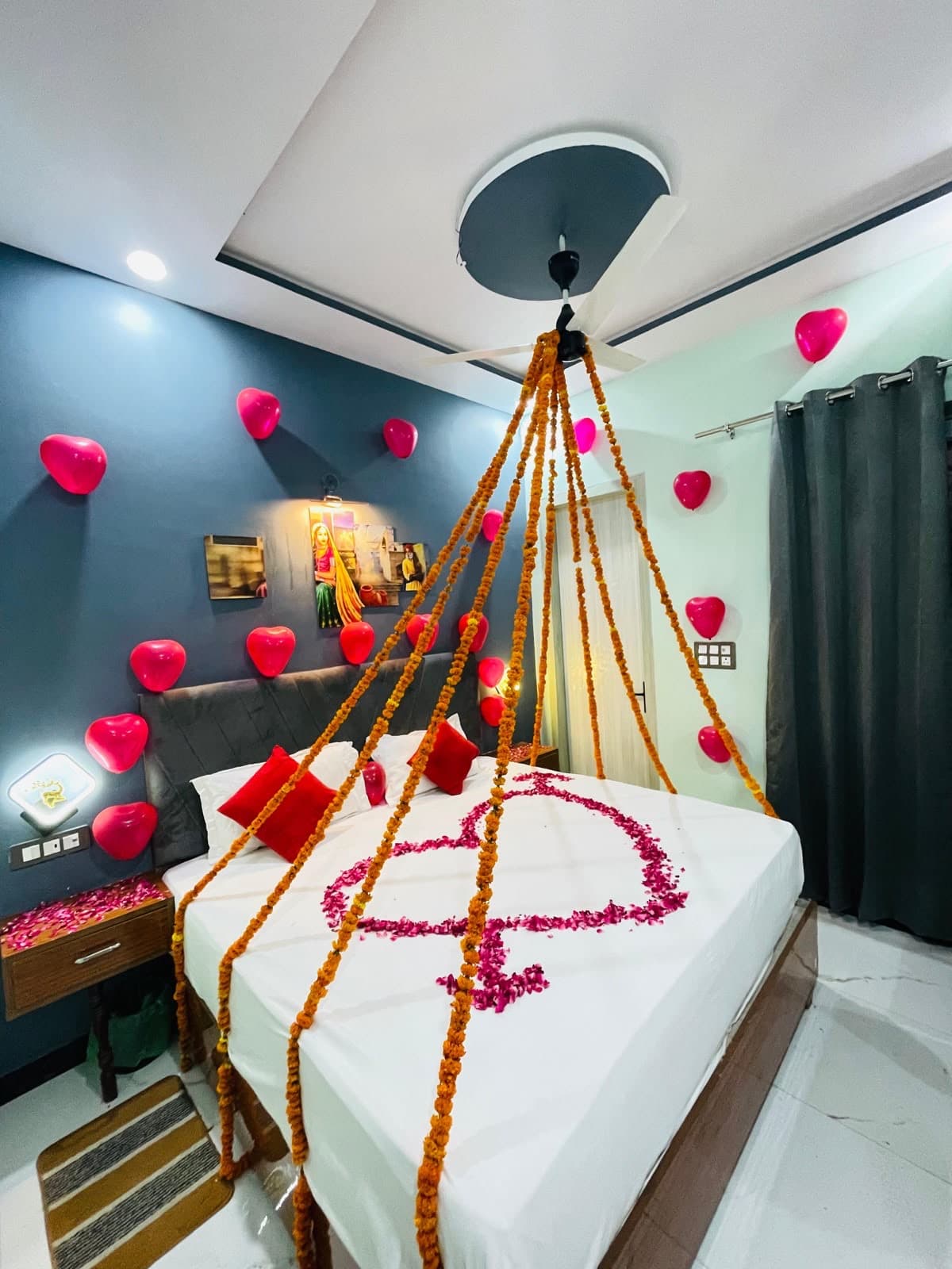 Romantic room decoration — heart balloons, marigold garlands and rose petals on bed